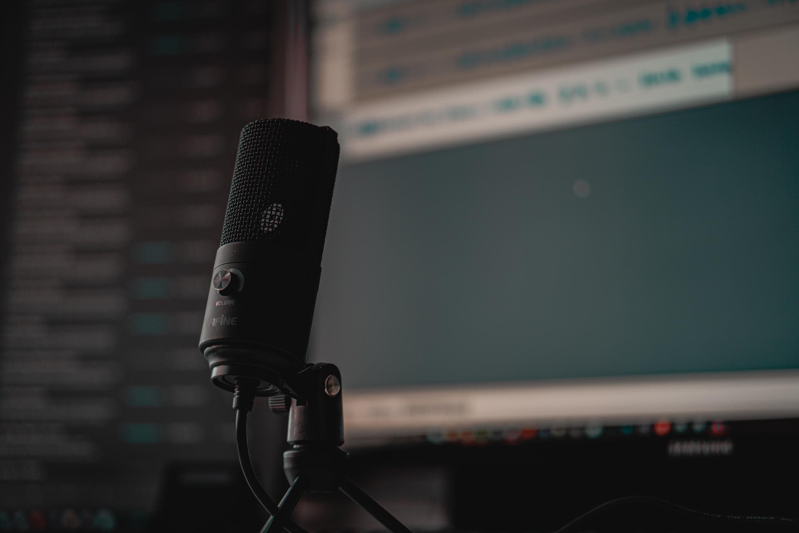 Black podcasting microphone with monitor in the background showing Audacity