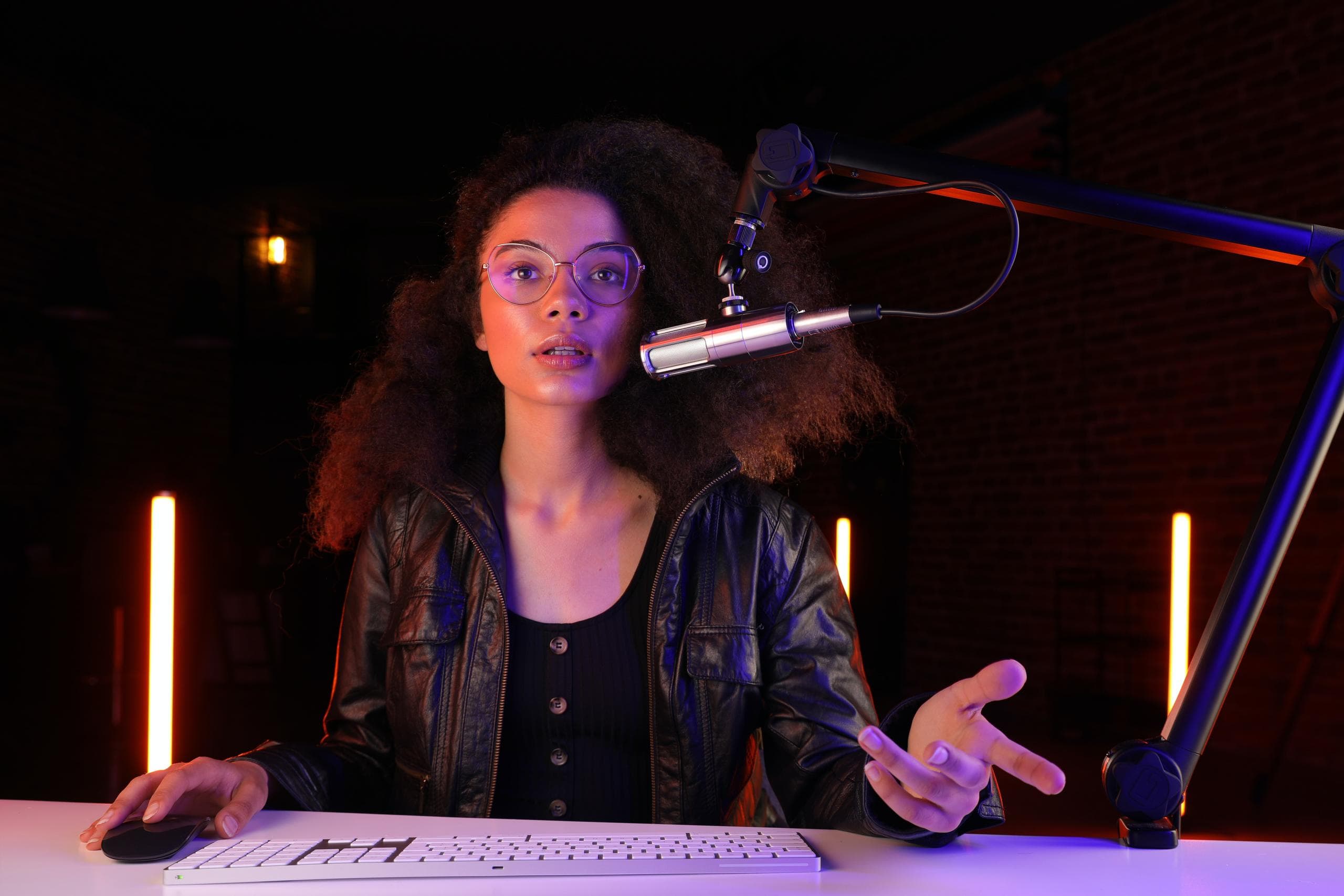 Woman with glasses in front of a computer with a podcasting microphone