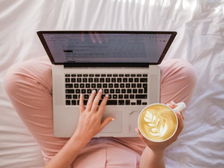 Woman with pink pants drinking coffee while working on a laptop. Over head shot.