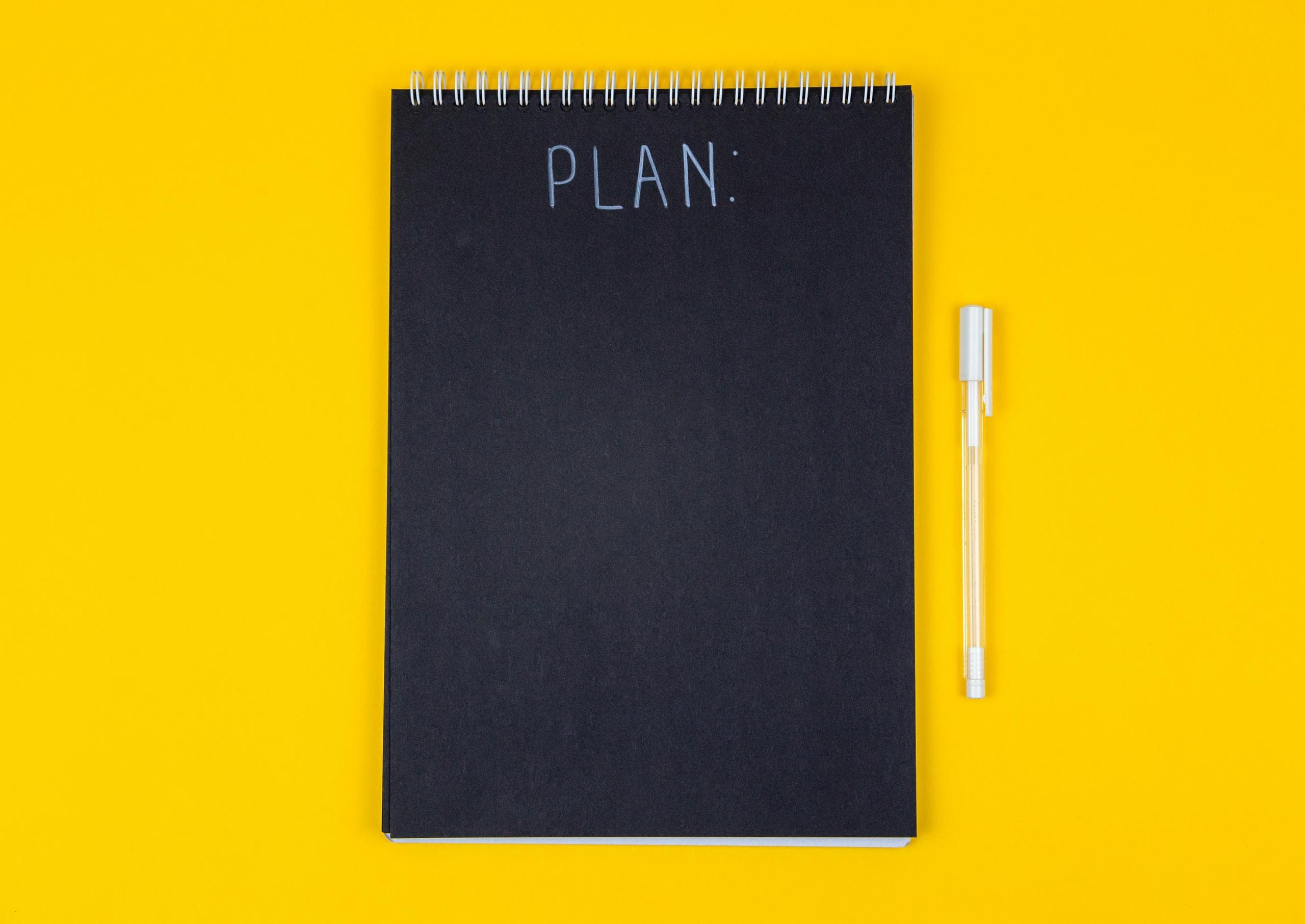 Black notebook on yellow background with a pen next to it